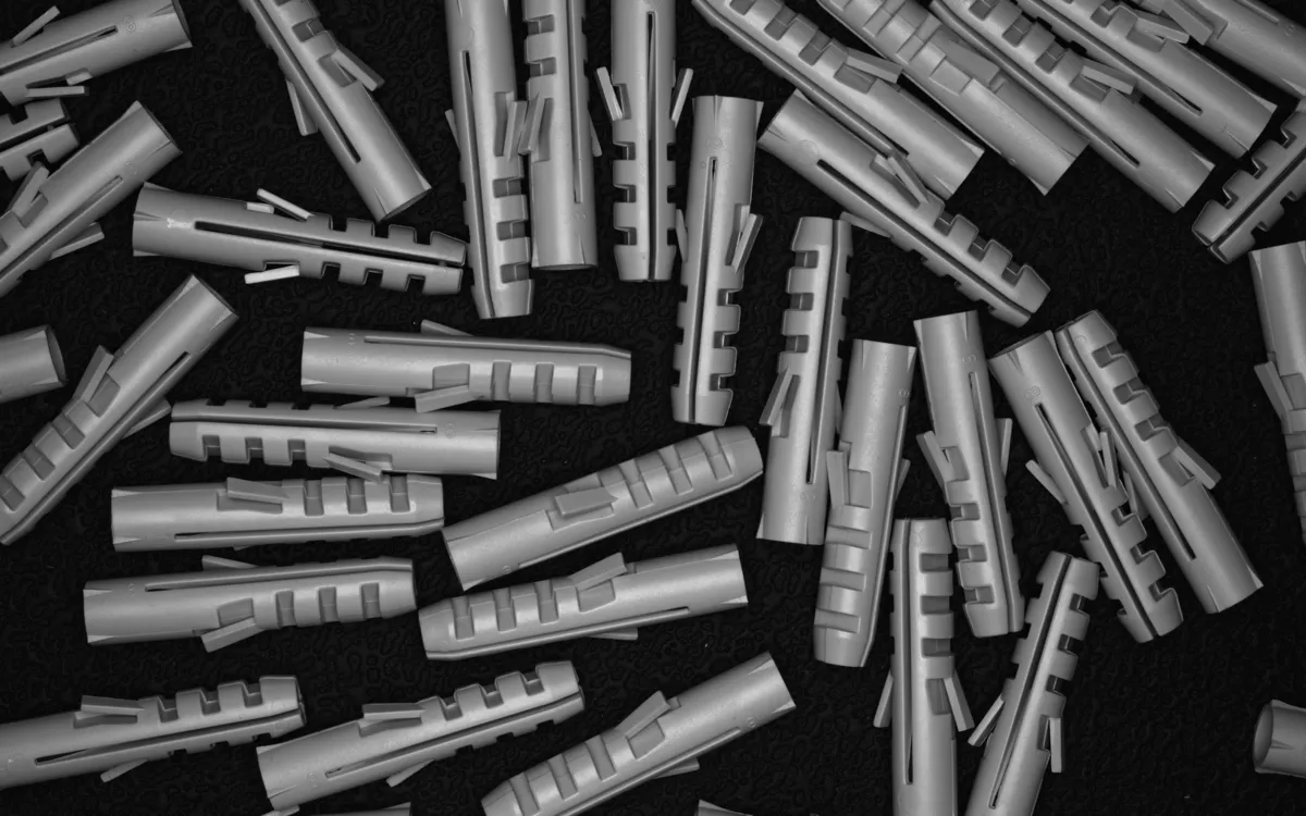 Grey plastic wall plugs scattered on a black background